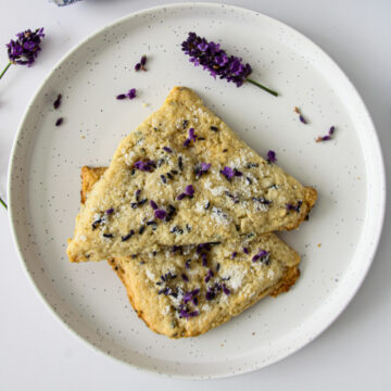 Two triangular shaped lavender scones on a white plate.