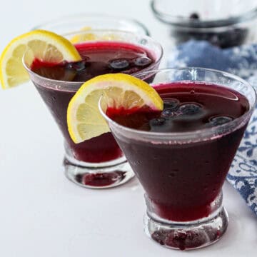 Two blueberry martini cocktails in stemless martini glasses.