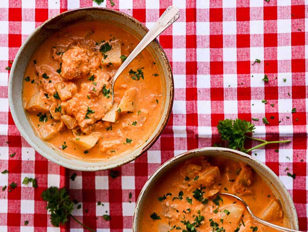 Two bowls of soup with spoons in them on a table
