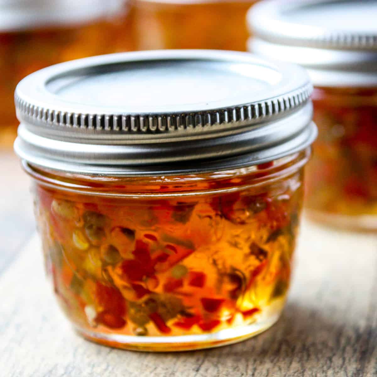A jar of pepper jelly on a wooden board.
