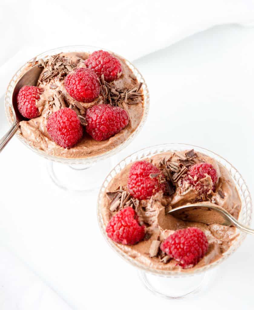 Two glass dessert dishes of raspberry chocolate mousse, one with a spoon in it.